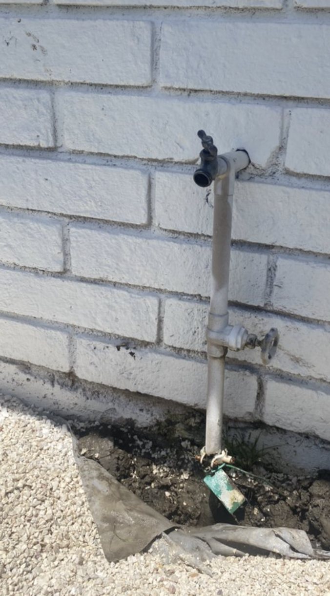 An old, corroded galvanized hose bibb and riser on an exterior brick wall before the repair
